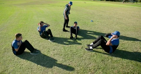 Male team with coach doing sit-ups on grass sports field, with colored cones, Stock Footage 341851463