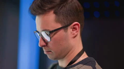 Male technician wearing glasses studies monitor reflection under blue LED studio Stock Footage 317543167