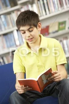 Male Teenage Student In Library Reading Book Stock Photos