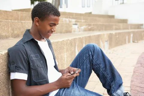 Male Teenage Student Sitting Outside On College Steps Using Mobile Phone Stock Photos