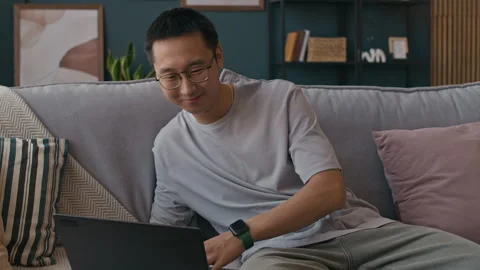 Male Teleworker Drinking Tea while Using Laptop Sitting on Home Couch Stock Footage 316295940