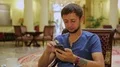 Male tourist sitting in hotel lobby with a coffee, reading news on mobile phone HD Footage