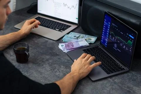 Male trader analyzing financial data on laptop with currency notes and coff.. Stock Photos
