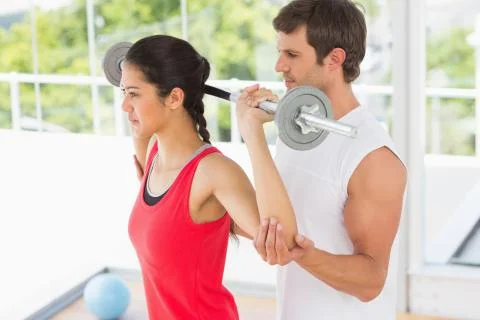 Male trainer helping fit woman to lift the barbell Stock Photos