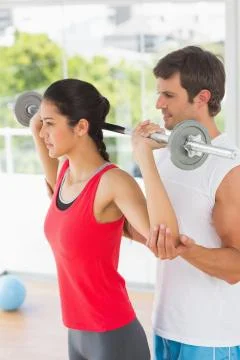 Male trainer helping fit woman to lift the barbell Stock Photos