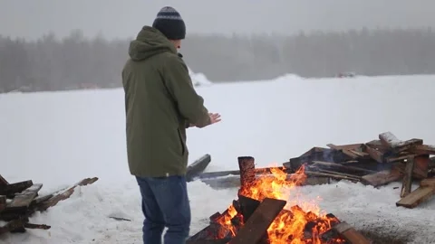 A male traveler basks in a fire in a snow-covered field in winter Stock Footage 146445824