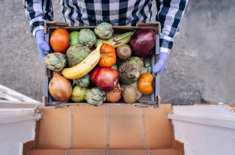 Male volunteer holding a box of fruits and vegetables in a house stairs. Stock Photos