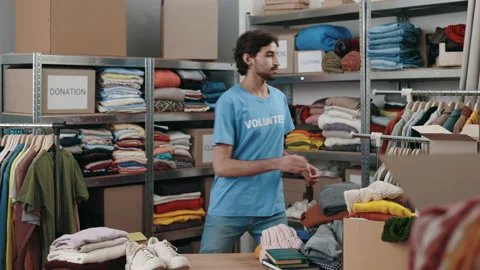 Male volunteer sorting and iterating clothes for donations at the warehouse.He Video stock 217983030