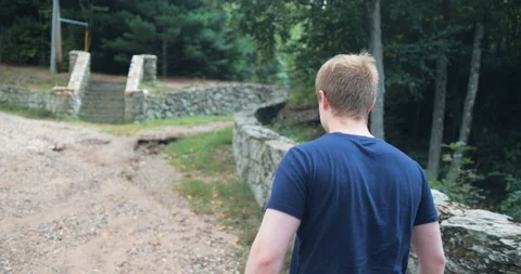 Male walking to rock wall and stairs on green forest trail Stock Footage
