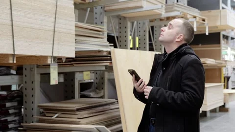 Male warehouse worker checking inventory on smartphone, standing near plywood Stock Footage 338217831
