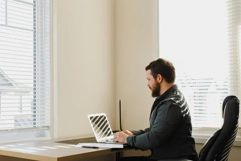 Male web developer sitting at desk and using laptop at cabinet. Stock Photos