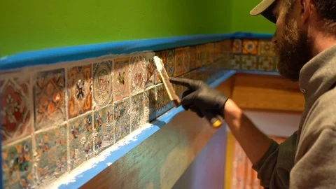 Male worker applying grout to a row of colorful tiles. Stock Footage 101434685