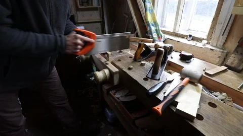 Male worker cutting the pine plank with a hand saw on the wooden workbench in a 库存影片 119670242
