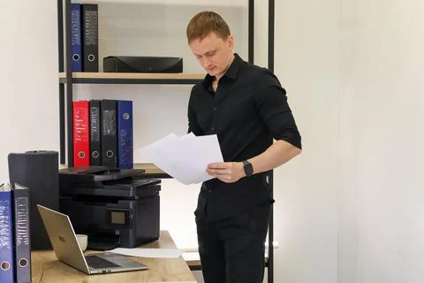Male worker examining stack of papers by printer Foto stock