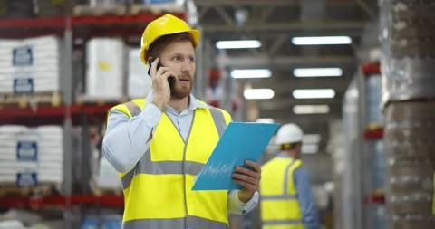 Male worker looking at clipboard while talking on mobile phone in warehouse. Stock Footage 151404749
