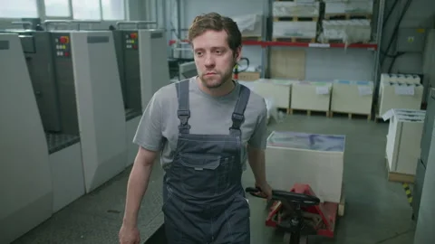 Male Worker Pulling Pallet Truck with Paper Material in Printing Factory Stock Footage 335483508