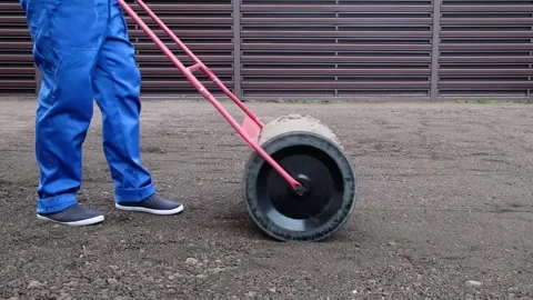 Male worker in a uniform prepares a plot of land for sowing  lawn roller Stock Footage 290166345