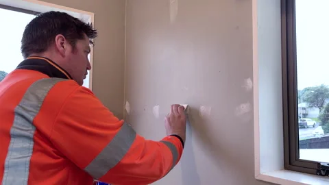 Male worker using a gap putty to fill holes in a wall before it's painted Stock Footage 281037361