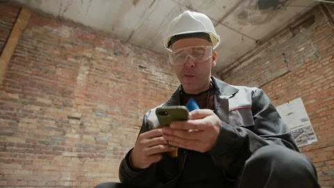 Male Worker Using Smartphone while Eating Sandwich at Construction Site Stock Footage 308920327