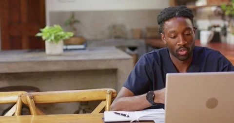 Man in 20s navy responding to laptop call at dining table, checking notes, Stock Footage 340988174