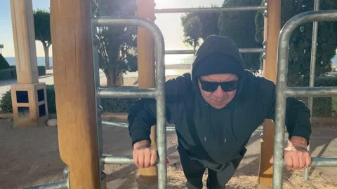 Man 50+ doing push-ups on outdoor exercise machine Stock Footage 328363857