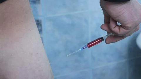 A man is about to inject himself with a red substance Stock Photos