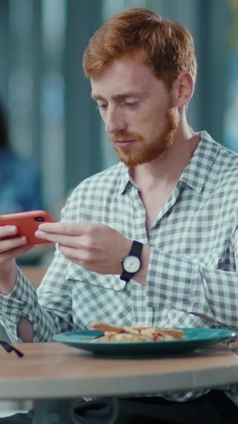A man is absorbed in his phone at a table with food, showing distraction Stock Footage 314962853