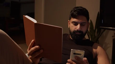 Man is Absorbed By Phone Ignoring Book in Other hand. Mid Shot Dolly Stockbeeldmateriaal 130155848