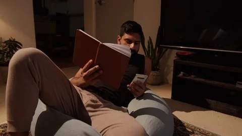 Man is Absorbed By Phone Ignoring Book in Other hand. Wide Shot Dolly Stockbeeldmateriaal 130155859