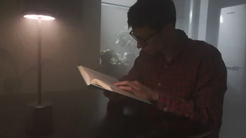 Man absorbed in reading book at night, lifestyle setting, warm cozy light. 스톡 동영상 318443591