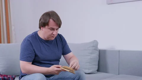Man absorbed in thoughtful examination of object while seated indoors on couch Stock Footage 311901075