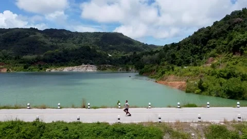 A man accelerates and quickly runs along the road along the lake Stock-Footage 167991179