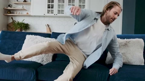 A man with acceleration jumps on a comfortable sofa at home and enjoys relaxing Stock Footage 196103306