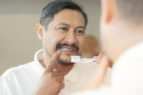 Man with aching teeth and brush while looking in mirror in bathroom. Stock Photos