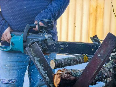Man actively using an electric chainsaw to cut tree branches and logs into 写真素材