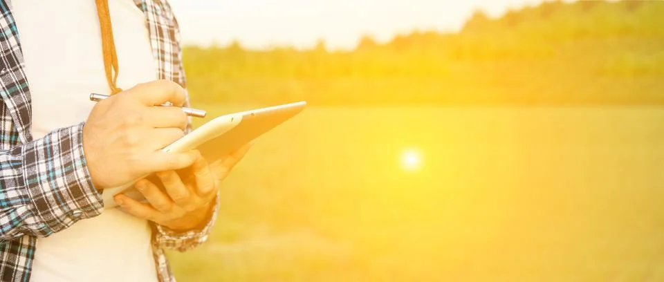 A man is actively using a tablet in a sunny field, symbolizing technologica.. Stock Photos