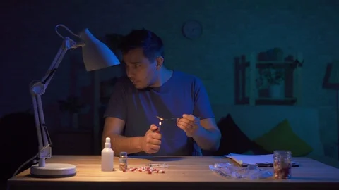 Man addict in a dark room at a table preparing for injection Stock Footage 106267057