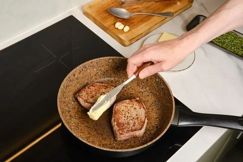 Man adding butter to frying pan with beef steaks Foto stock