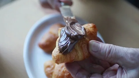 Man adding chocolate spread to croissant Stock Footage 89347488