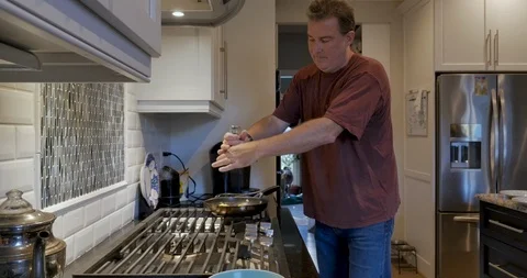 Man adding fresh ground pepper and salt to a frying pan on a gas stove Stock Footage 109072791