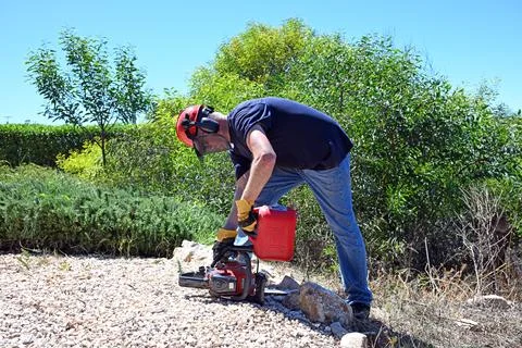 Man adding fuel from a plastic fuel can to his chain saw Stock Photos