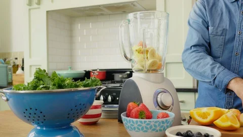 Man Adding Nutritious Fruits And Water In Blender On Table Stock Footage 86073916
