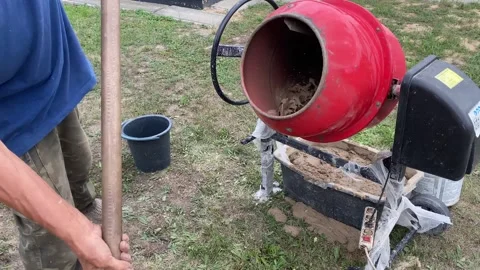 Man adding sand to red cement mixer with water and clay inside Stock Footage 316539416
