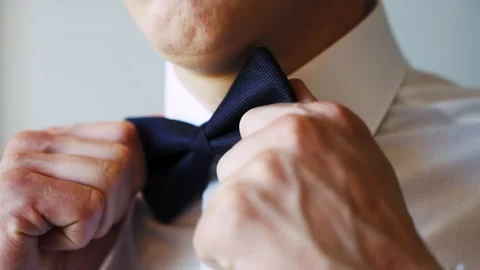 The man adjusted the dark blue bow tie on his white shirt with his hands. Vidéo 285346444