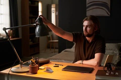 Man Adjusting Desk Lamp for Remote Work in Home Office Stock Photos