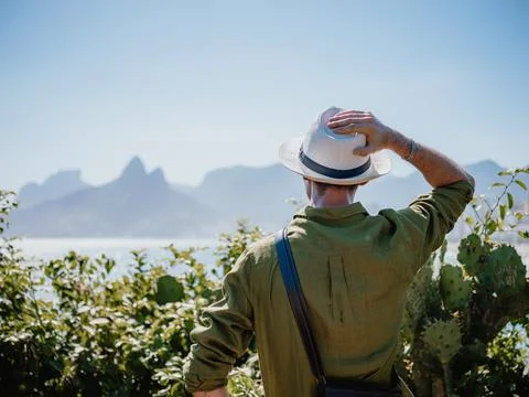 Man adjusting hat while looking at sea and mountains Stock Photos