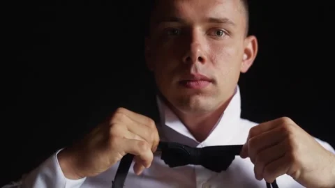 Man adjusting his bow tie on a black background Stock Footage 242427492
