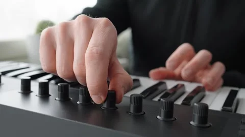 Man adjusting the knobs on a keyboard while playing it next to a window 스톡 동영상 304214451
