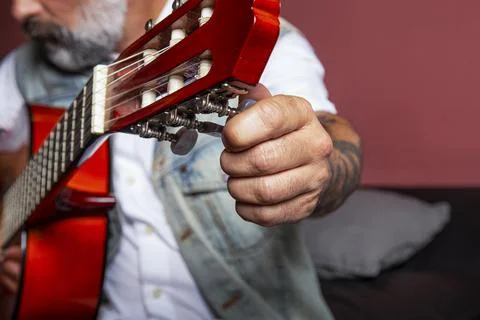 Man adjusting the nodes of the guitar while sitting on the sofa. Stock Photos
