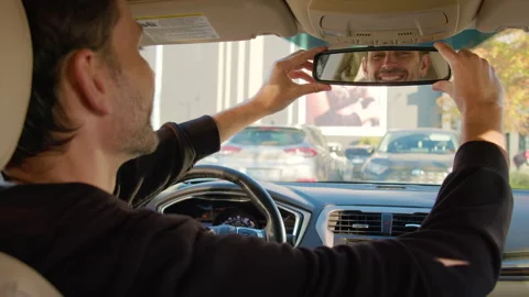 Man adjusting rearview mirror in car, showcasing focus on safety and awareness Stock Footage 316834847